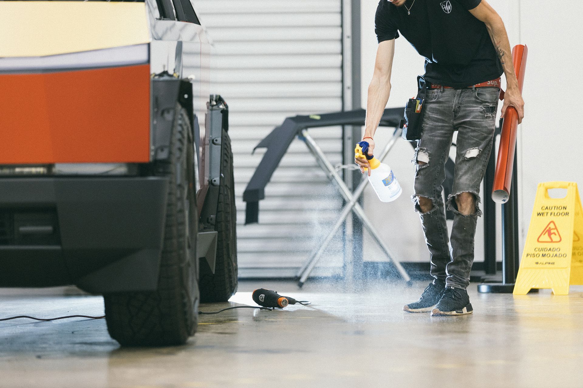 Man spraying liquid on floor near a car, likely preparing for detailing.