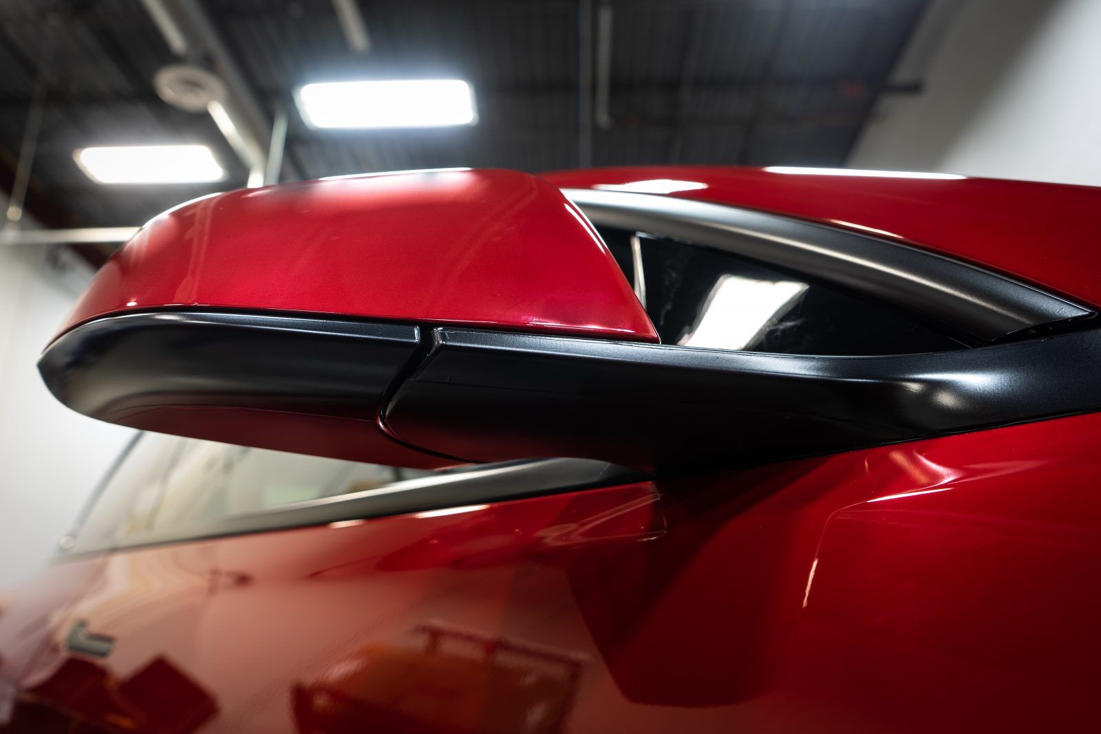 Red car side mirror, black trim, reflective, indoors.