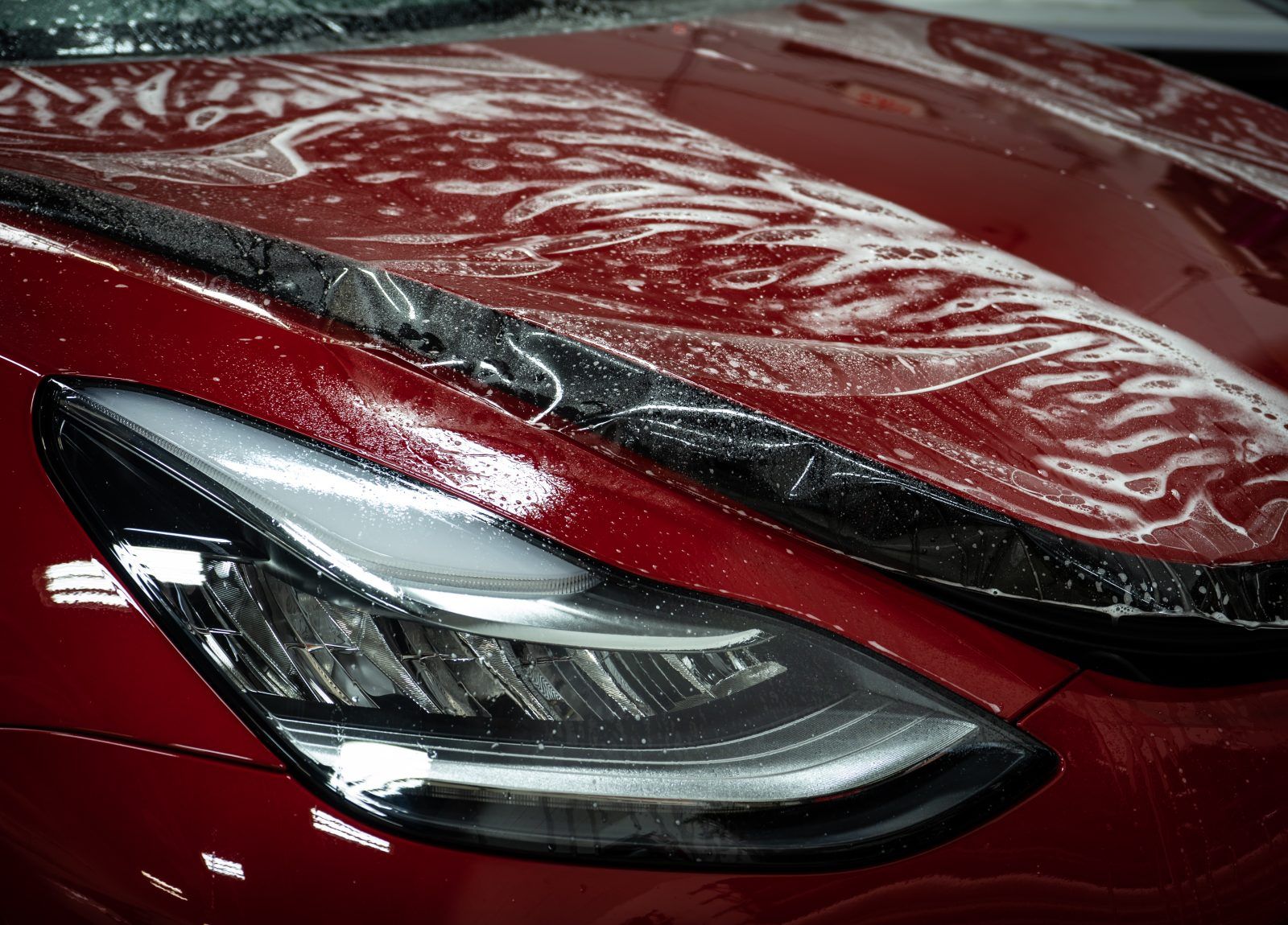 Red car hood with protective film over it, visible headlight.