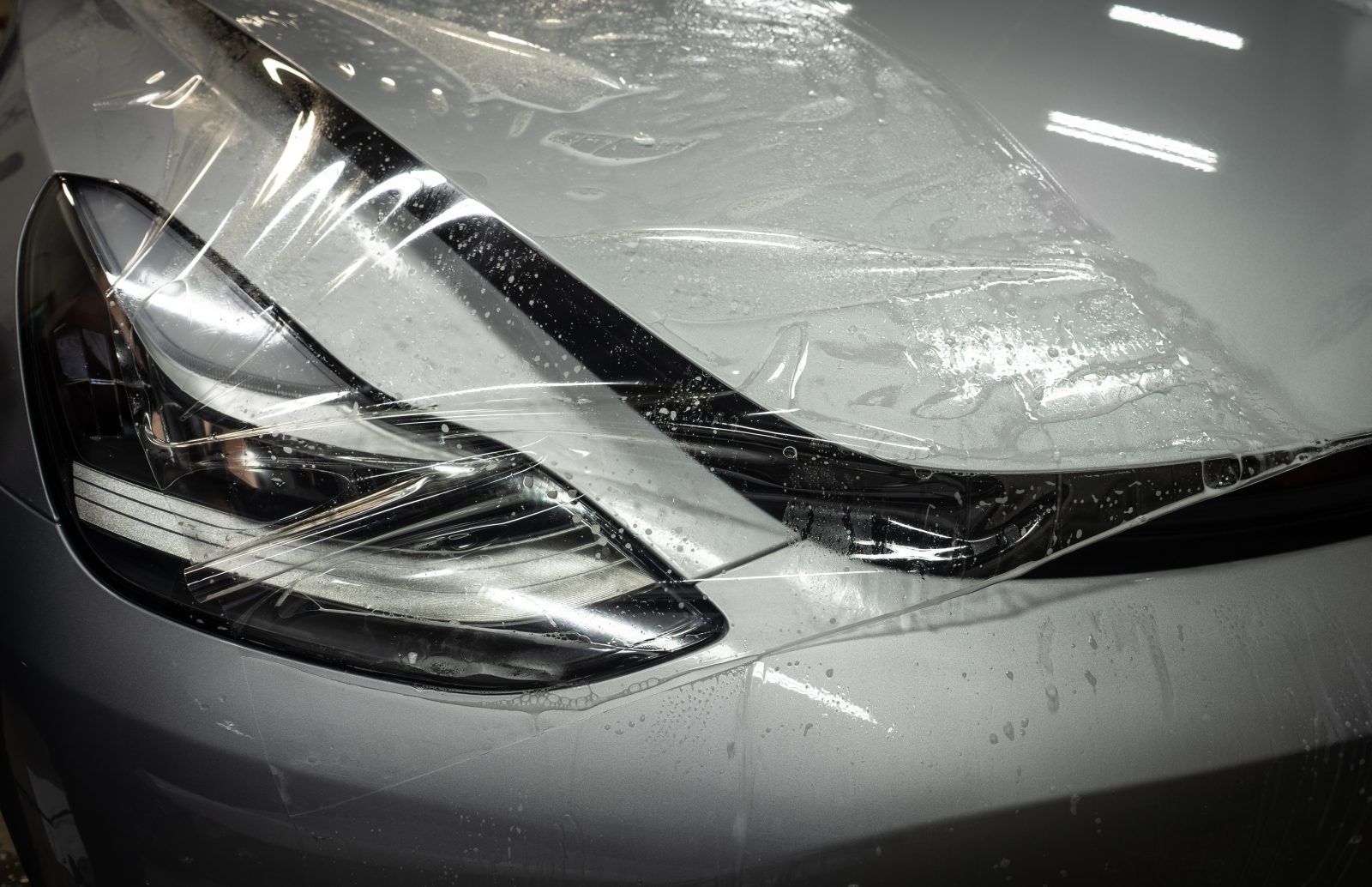 Car headlight and front hood covered with clear protective film.