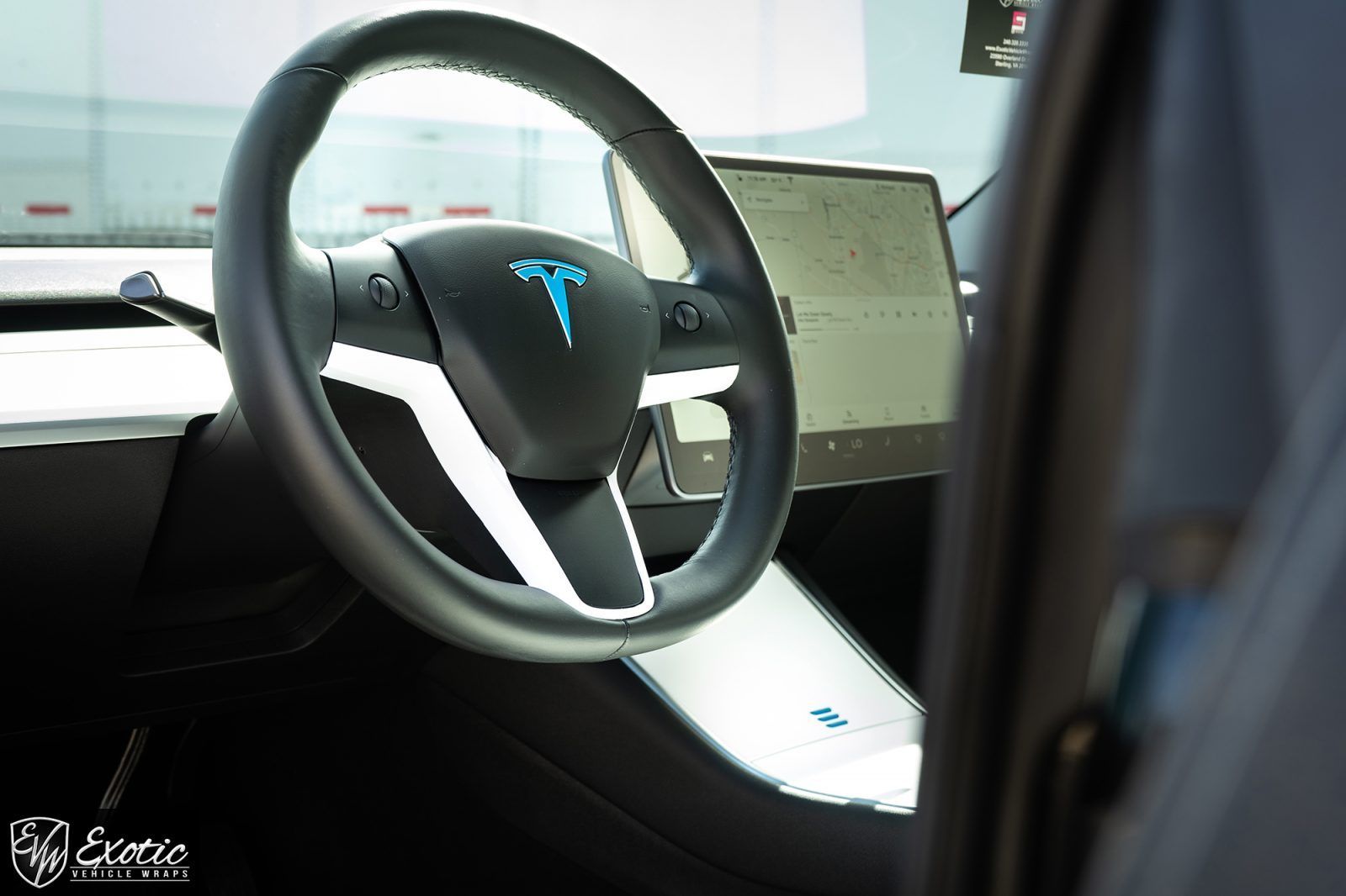 Tesla car interior: Steering wheel with blue logo, dashboard, touchscreen display.