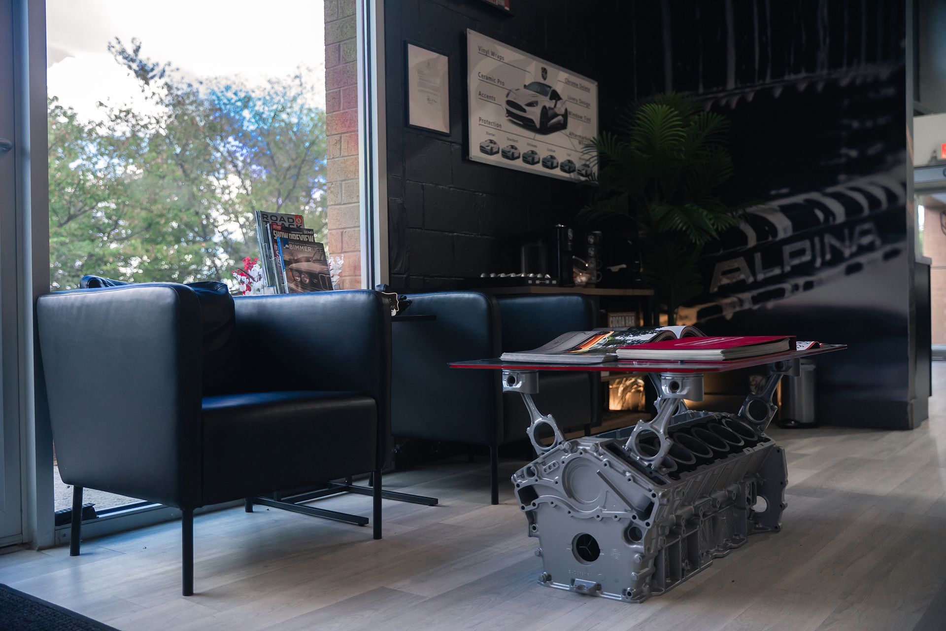 A waiting area with a black chair, table, and engine block. The window looks outside.