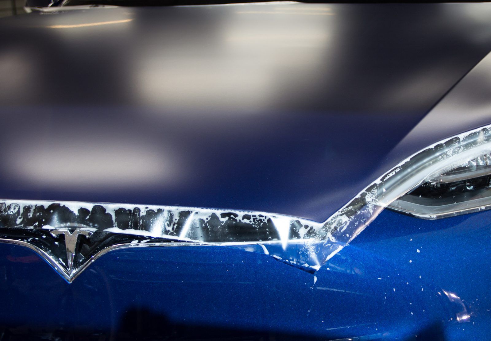 Blue car hood with dark film being applied, wet with soapy water.