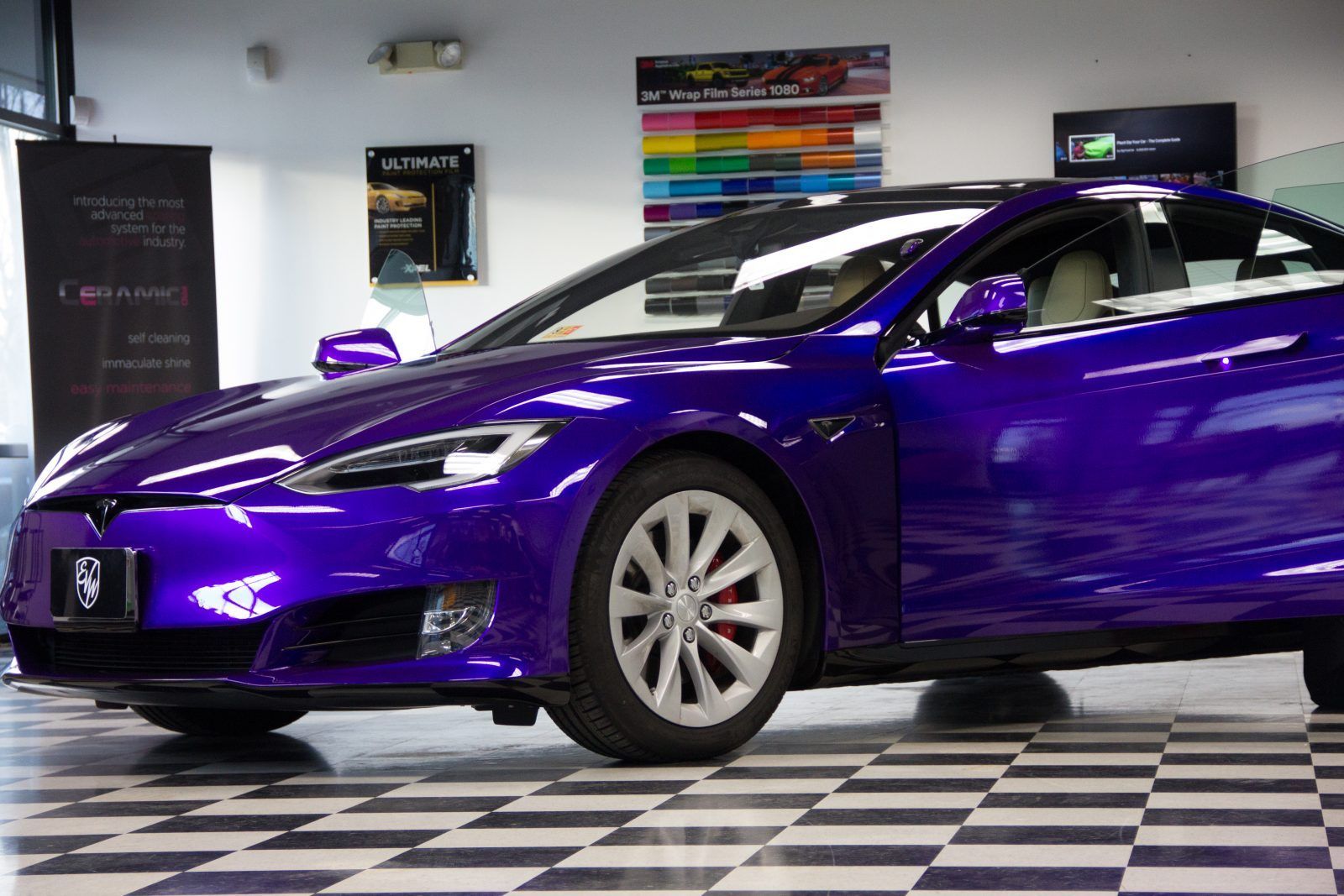 Purple Tesla car in a showroom, sitting on checkered floor.