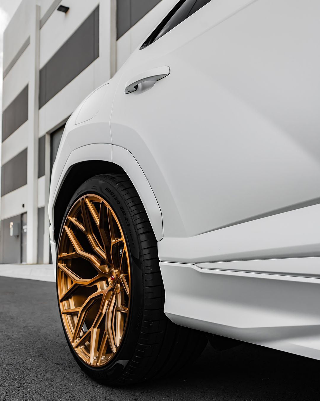 White car with gold rims, parked near a building.
