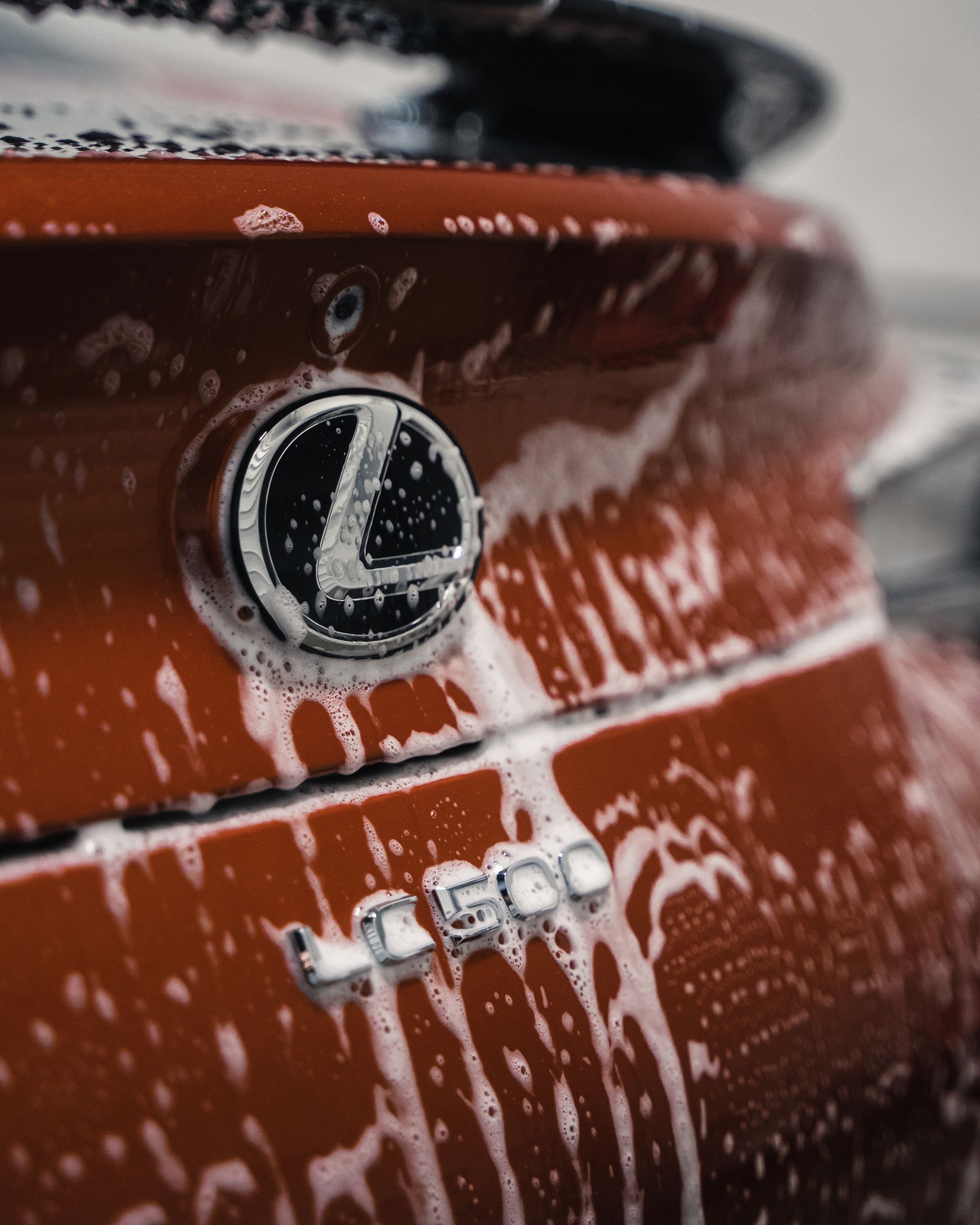 Red Lexus car with foamy soap suds, a chrome emblem and the number