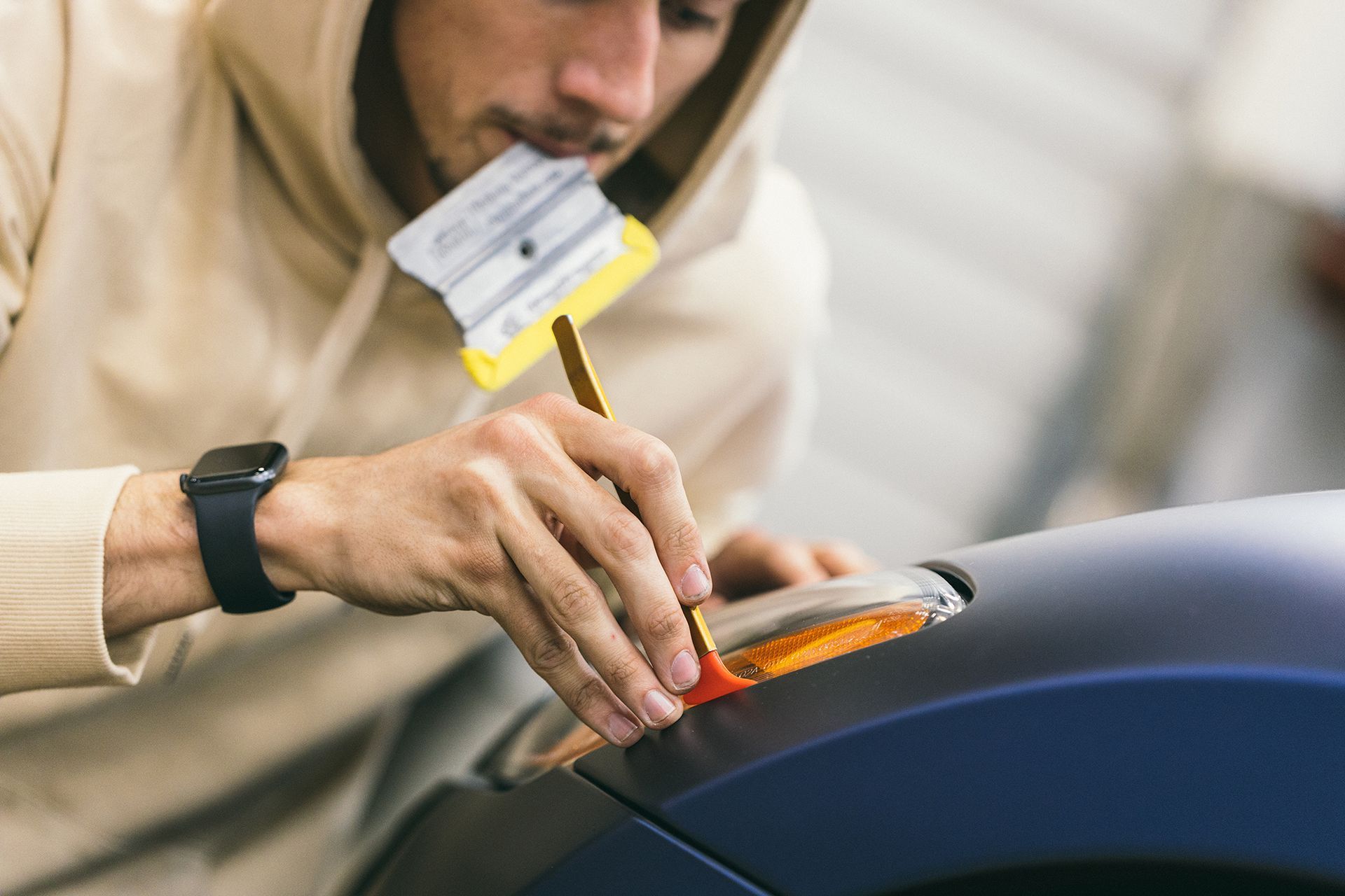 Man in hoodie applying film to car headlight with tool.