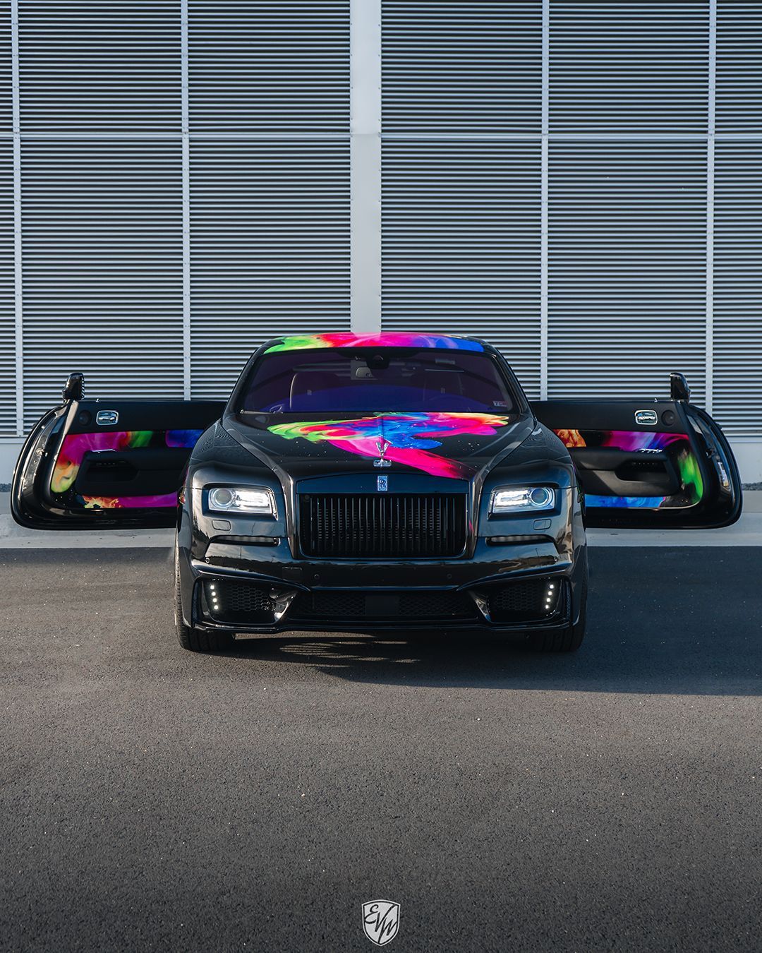 Black Rolls Royce with open doors, vibrant graffiti on exterior and interior.