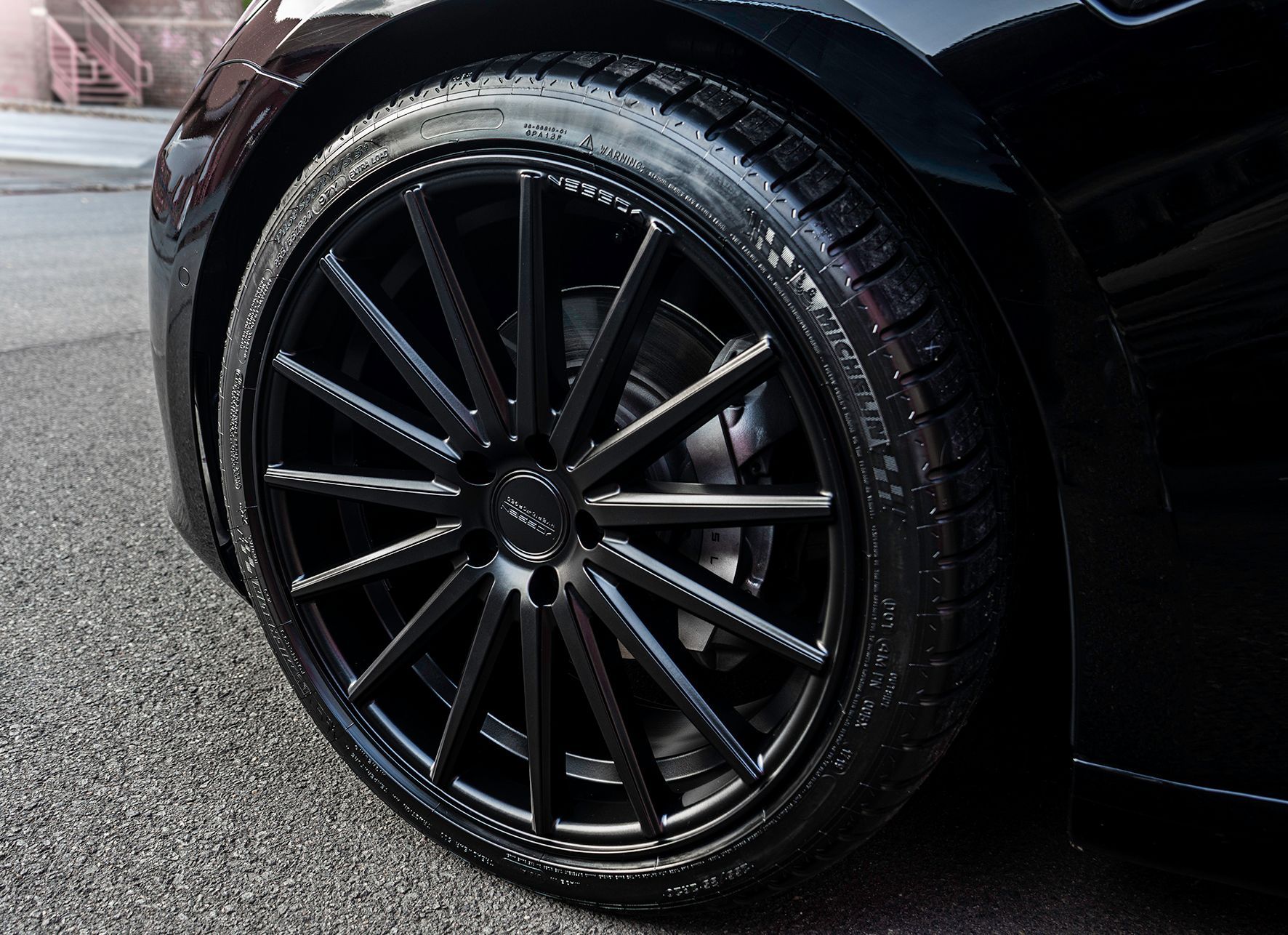 Black car wheel with black spokes and tire, on a wet, gray surface.