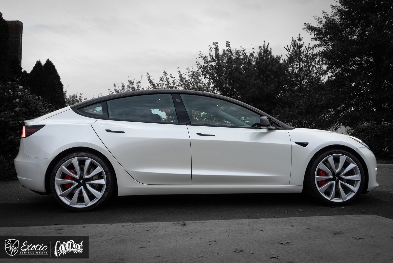 White Tesla Model 3 sedan parked on a street. Red brake calipers. Black roof and wheels.