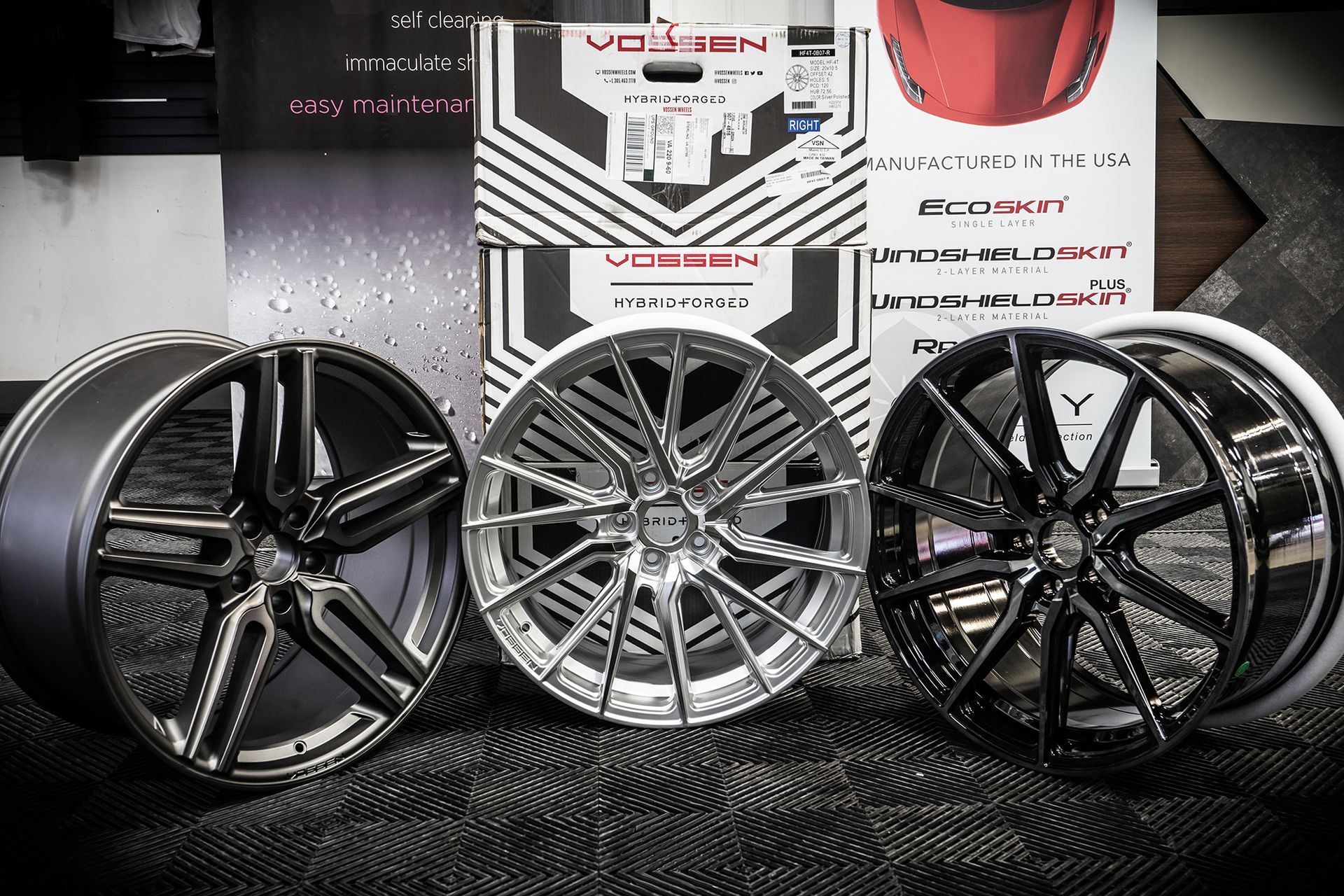 Three shiny car wheels in different finishes on a black surface, Vossen branded boxes in background.