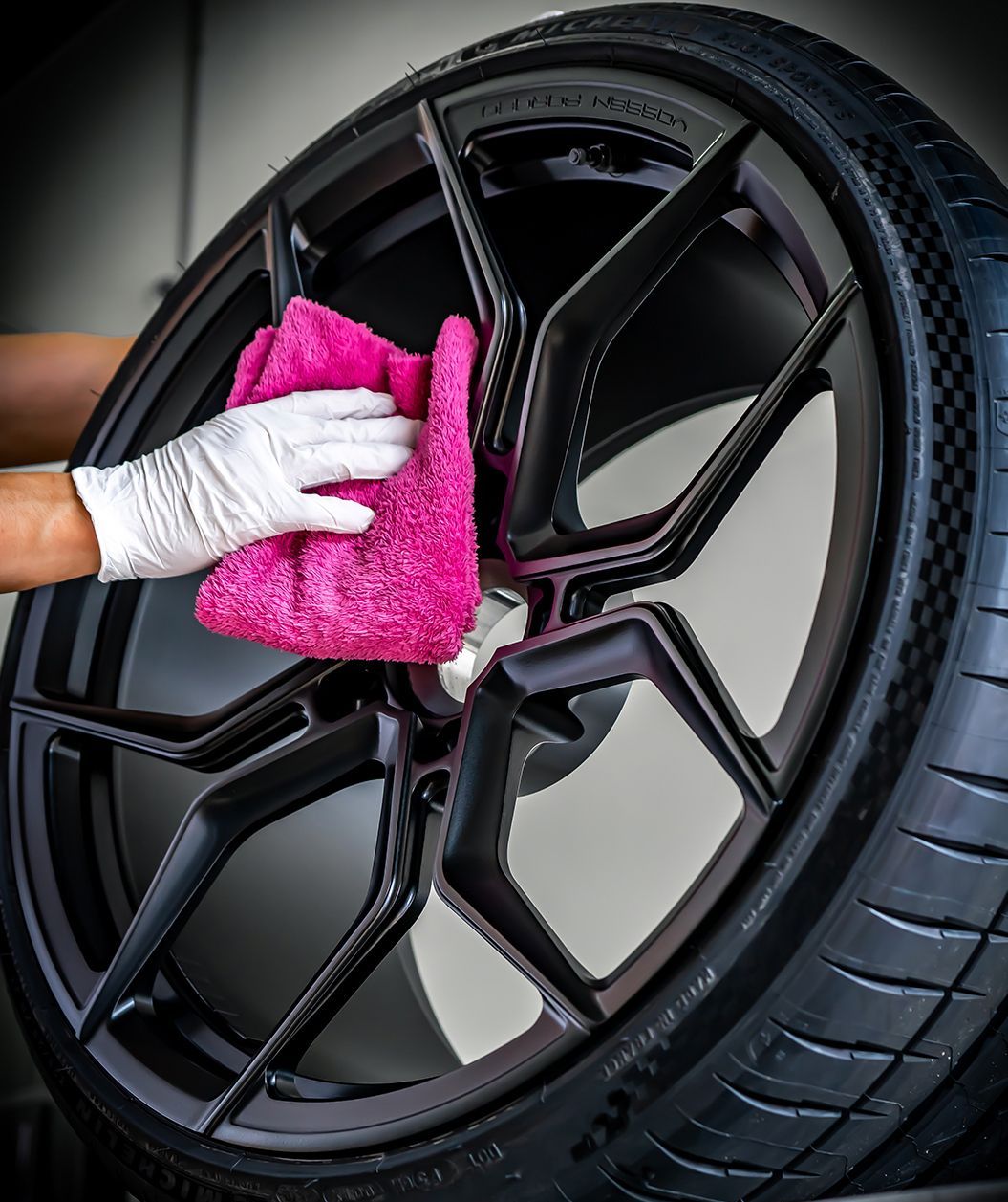 Person wearing a glove wiping a black car wheel with a pink cloth.