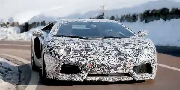 Camouflaged Lamborghini sports car driving on a road with snow-covered mountains in the background.