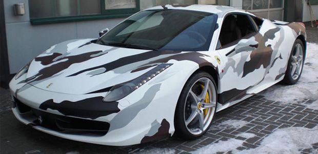 White Ferrari sports car with camouflage pattern in a snowy setting.