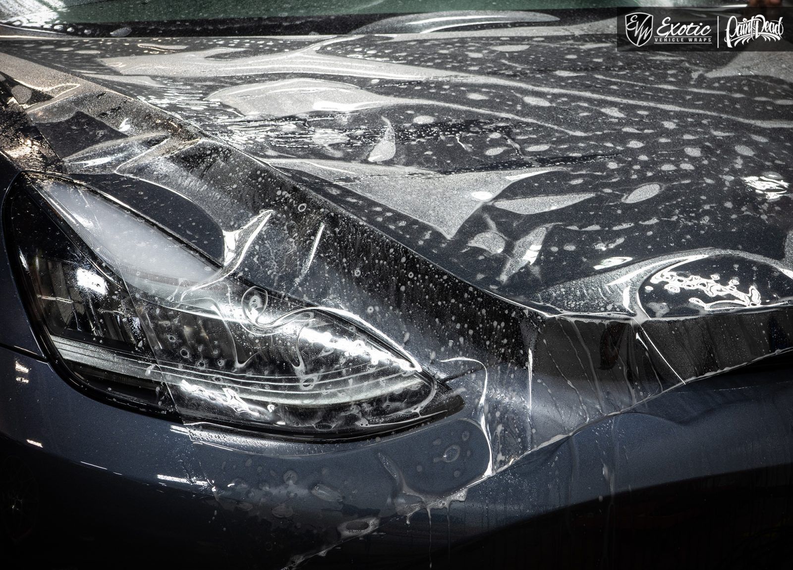 Car hood being covered in clear protective film, with water sprayed on it.