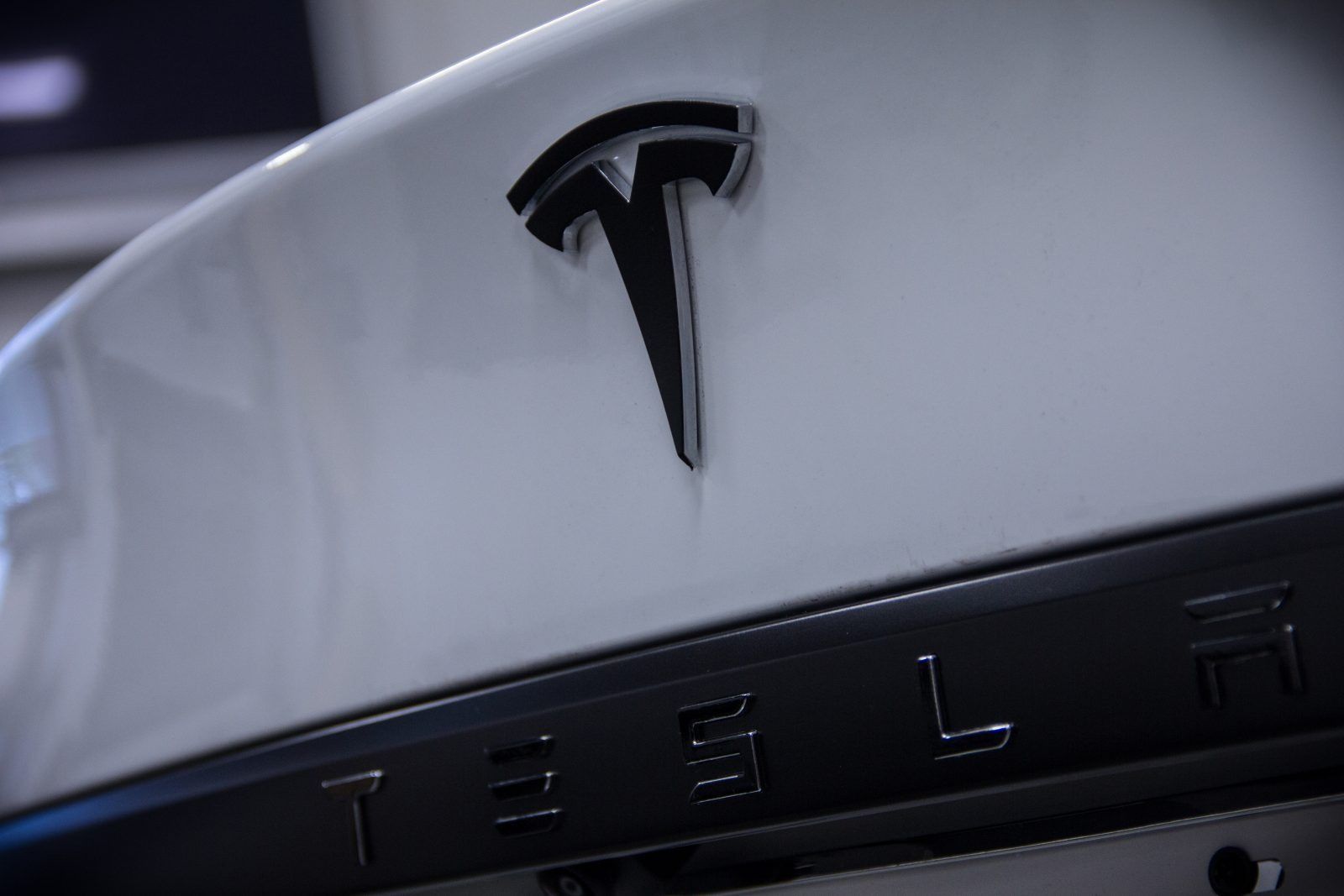 Close-up of a white Tesla car's rear with a black Tesla logo and lettering.