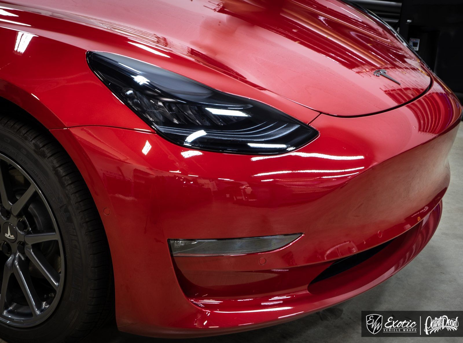 Red Tesla Model 3 car, front view, with a glossy finish, in a garage.