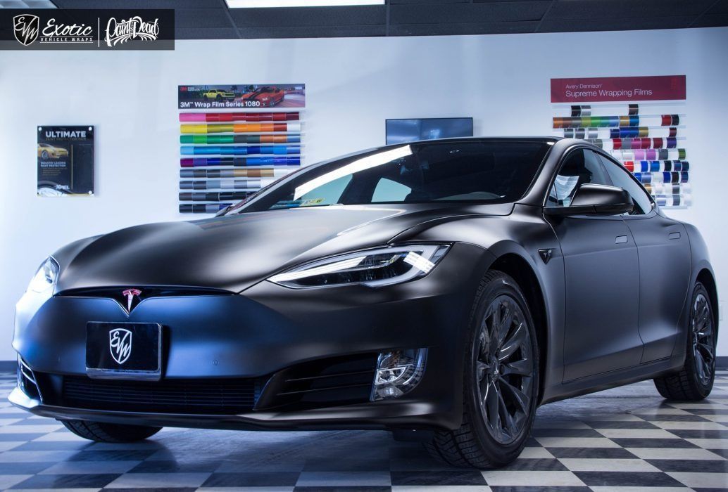 Black matte Tesla in a shop, with color samples on the wall.