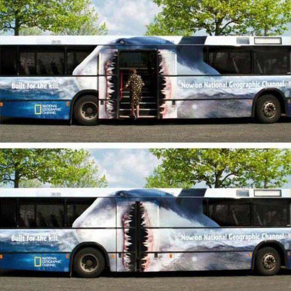 Bus with shark mouth graphic, door open. Person enters. National Geographic ad.