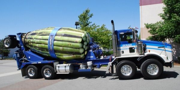 Cement truck with a vegetable wrap, parked in front of a building on a sunny day.
