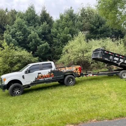 White truck with Jones Tree Service logo towing a trailer on green grass, trees in the background.