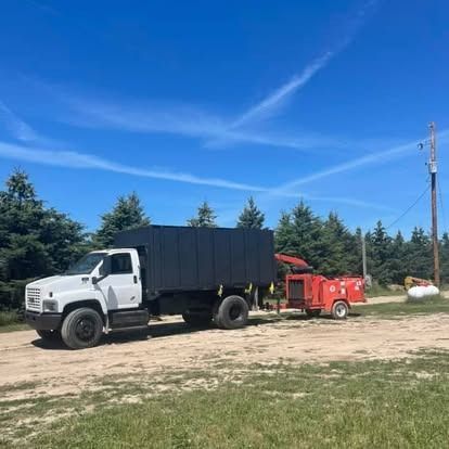 White truck with dark box body and red wood chipper on a dirt road under a blue sky.