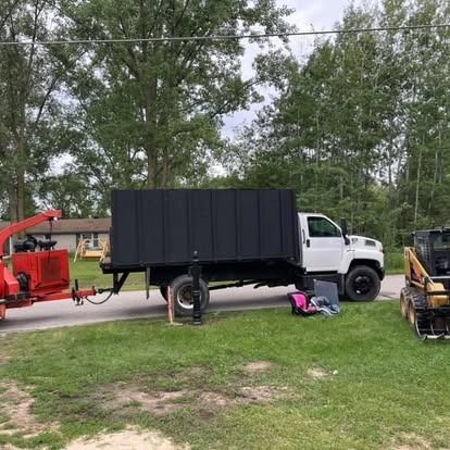White truck with black box bed, wood chipper, and skid steer on a grassy area.
