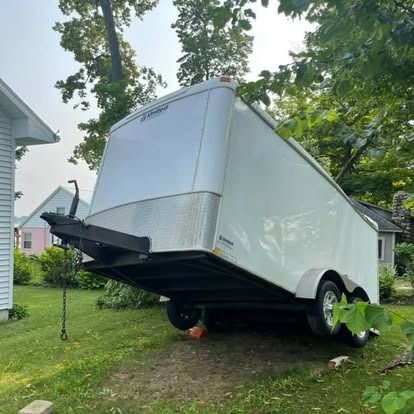 White enclosed trailer tilted on a grassy lawn.