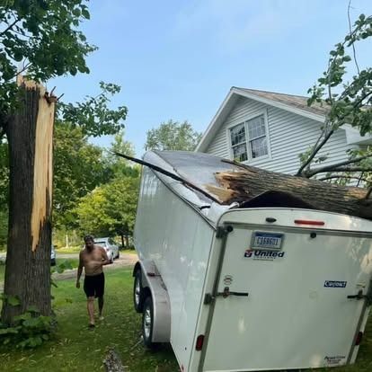 Man walking near a damaged trailer with a tree branch through it. The tree next to them is split.