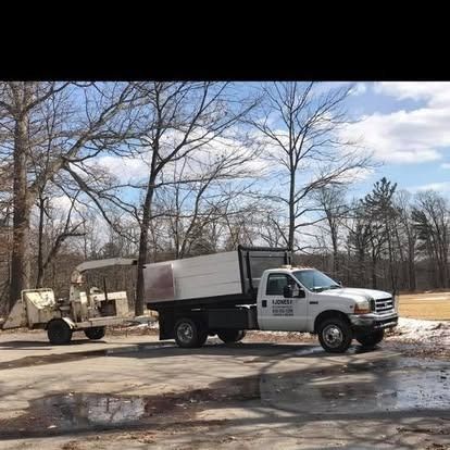 White truck with a tree chipper, parked in a wooded area.