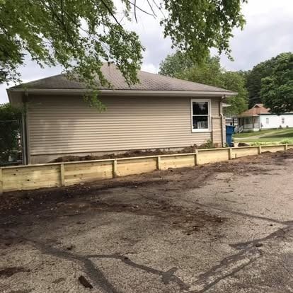 Tan building with newly built wooden garden beds in front, on a paved area, with trees.