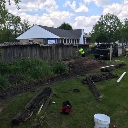 Workers removing an old wooden fence near a building. Mud and debris are scattered in the foreground.