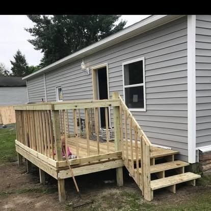 A wooden deck with stairs adjoins a gray house. A child plays on the deck.