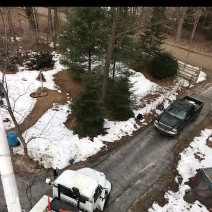 Aerial view: Truck driving on a snow-lined driveway, with a utility truck in the foreground and a wooded backdrop.