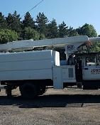 White utility truck with an extended boom, parked near trees.