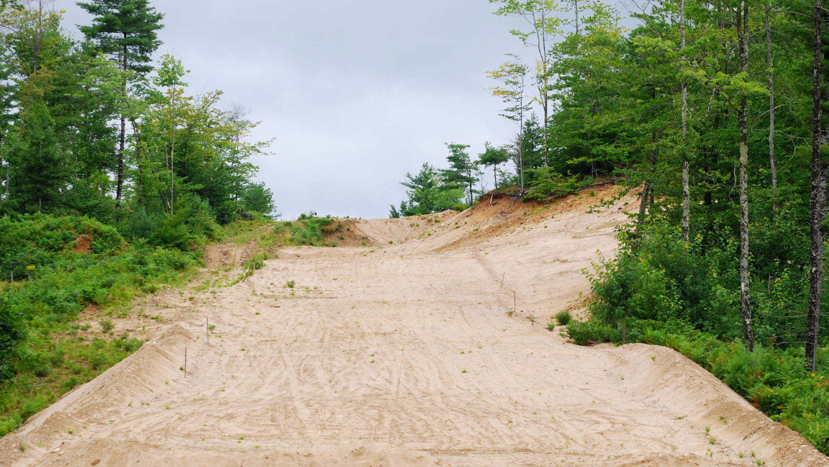 Dirt ramp up a hill with trees on either side and overcast sky.