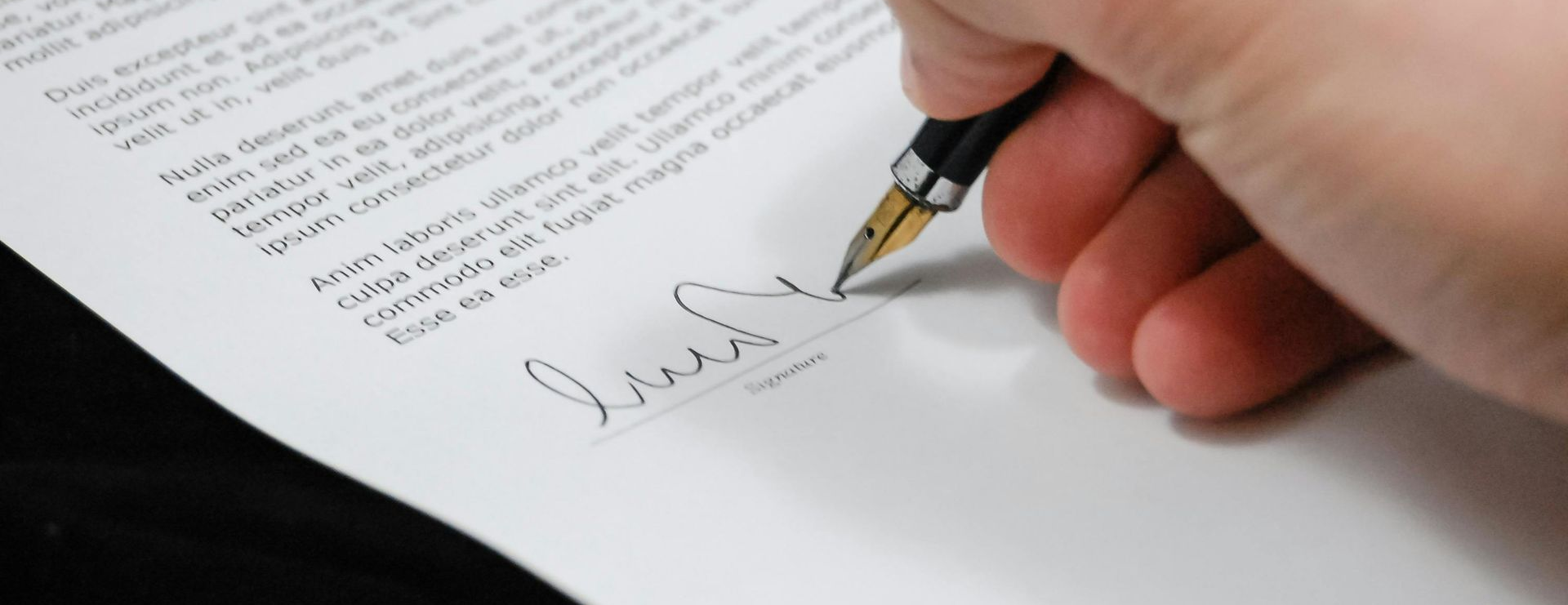 A hand holding a pen, signing a document.