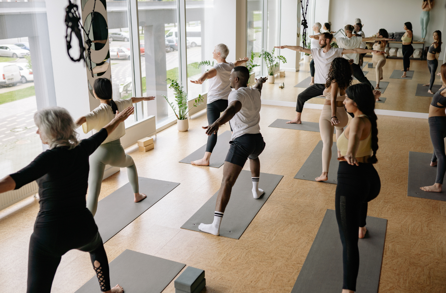 People in a yoga class, stretching on mats in a sunlit studio.