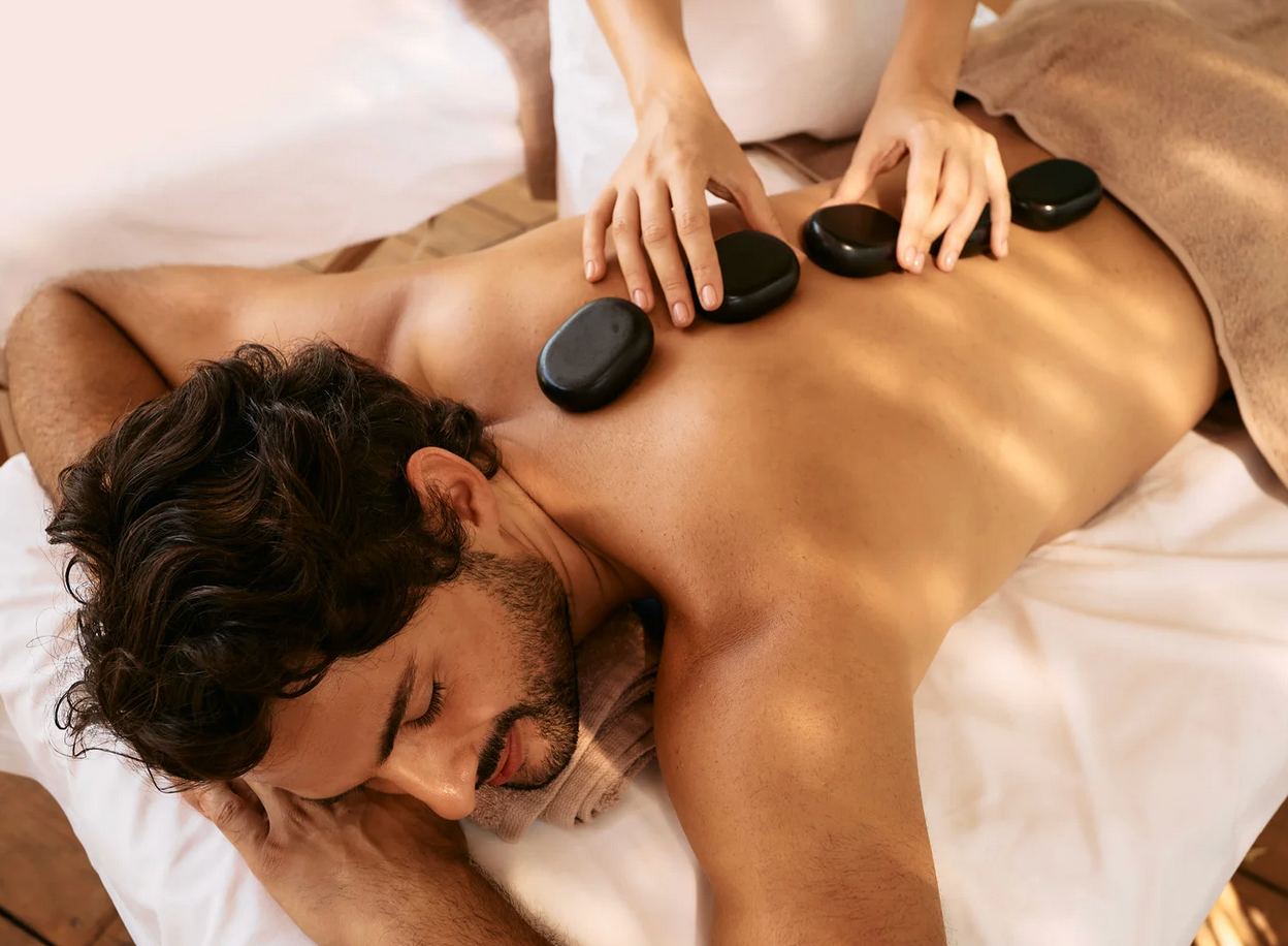 Man receiving hot stone massage on his back at a spa.