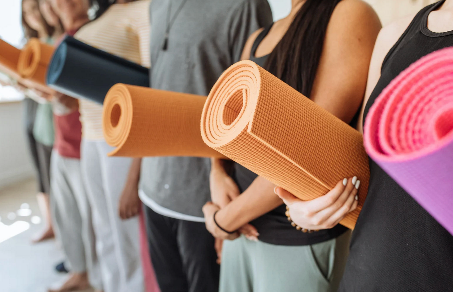 People standing in a line holding rolled-up yoga mats, ready for class.