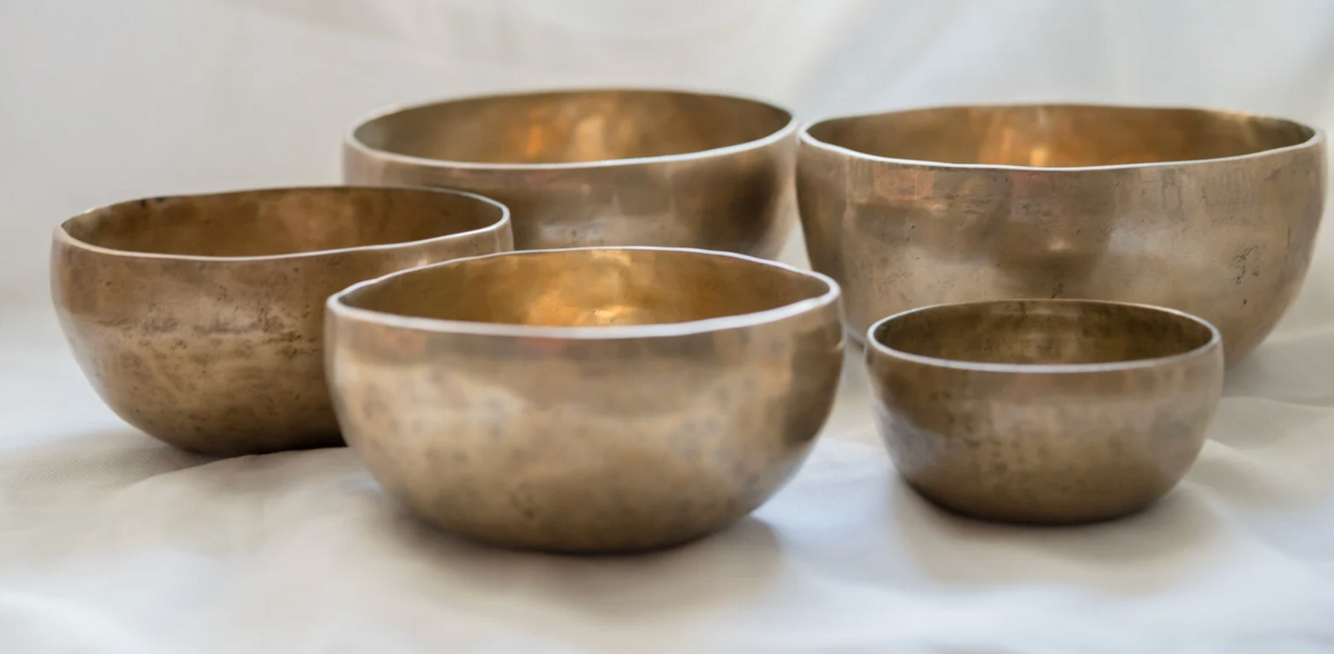 Five bronze singing bowls sit on a white surface.