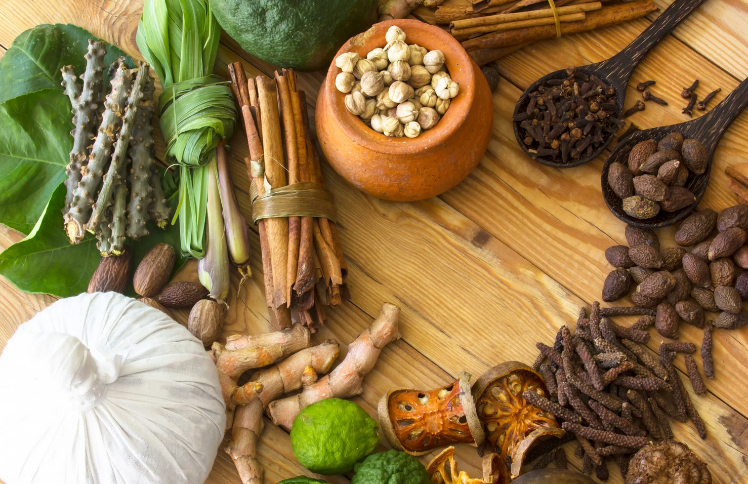 Assortment of aromatic herbs and spices, including cinnamon, cloves, and ginger, on a wooden surface.