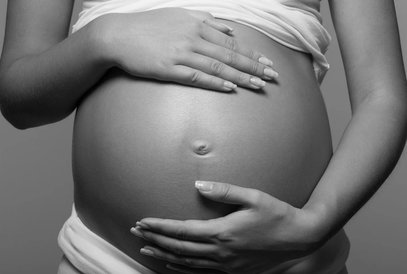 Pregnant woman's belly; hands cradling abdomen, black and white photo.