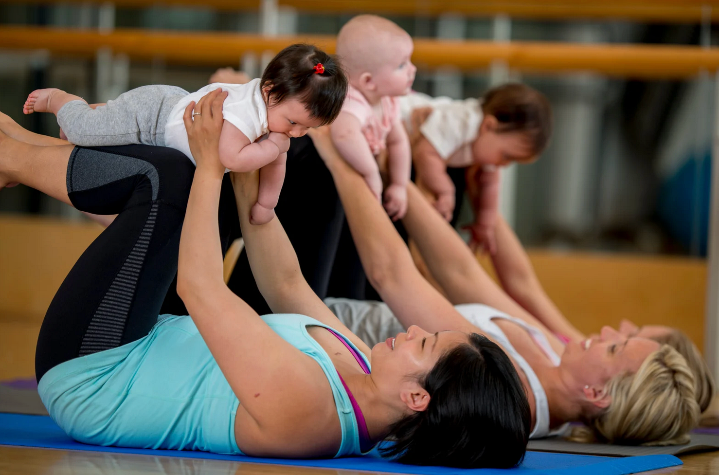 Mothers doing yoga with babies in a studio. Holding babies above their bodies, smiling.