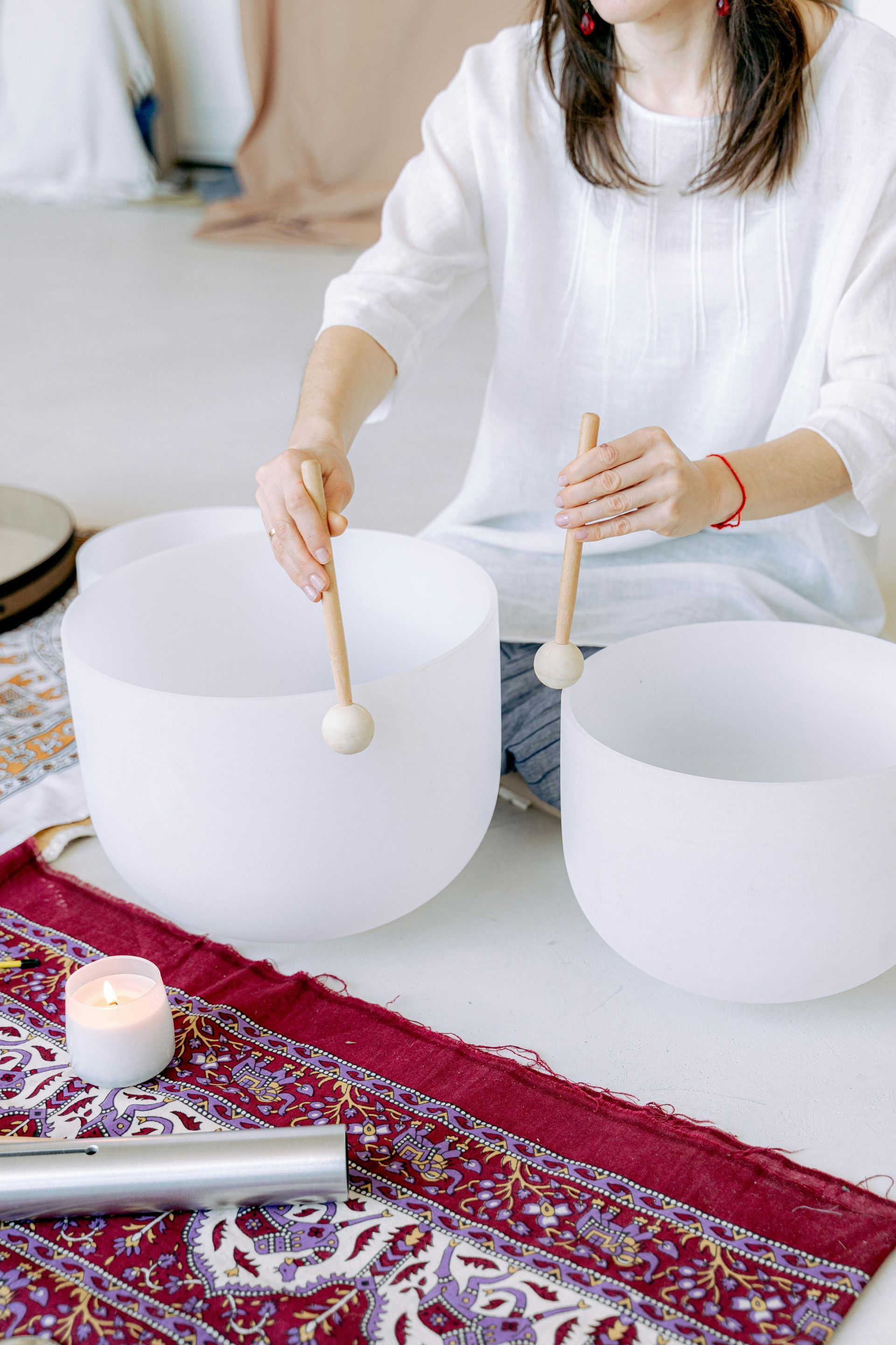 Woman plays crystal singing bowls, indoors. White top, red bracelet.