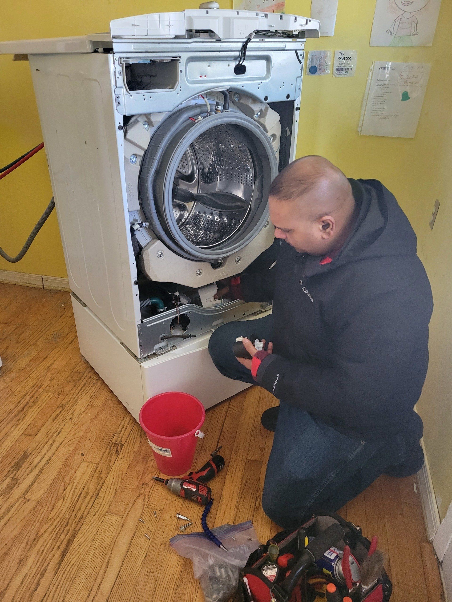 Full length of handyman checking washing machine with flashlight in kitchen