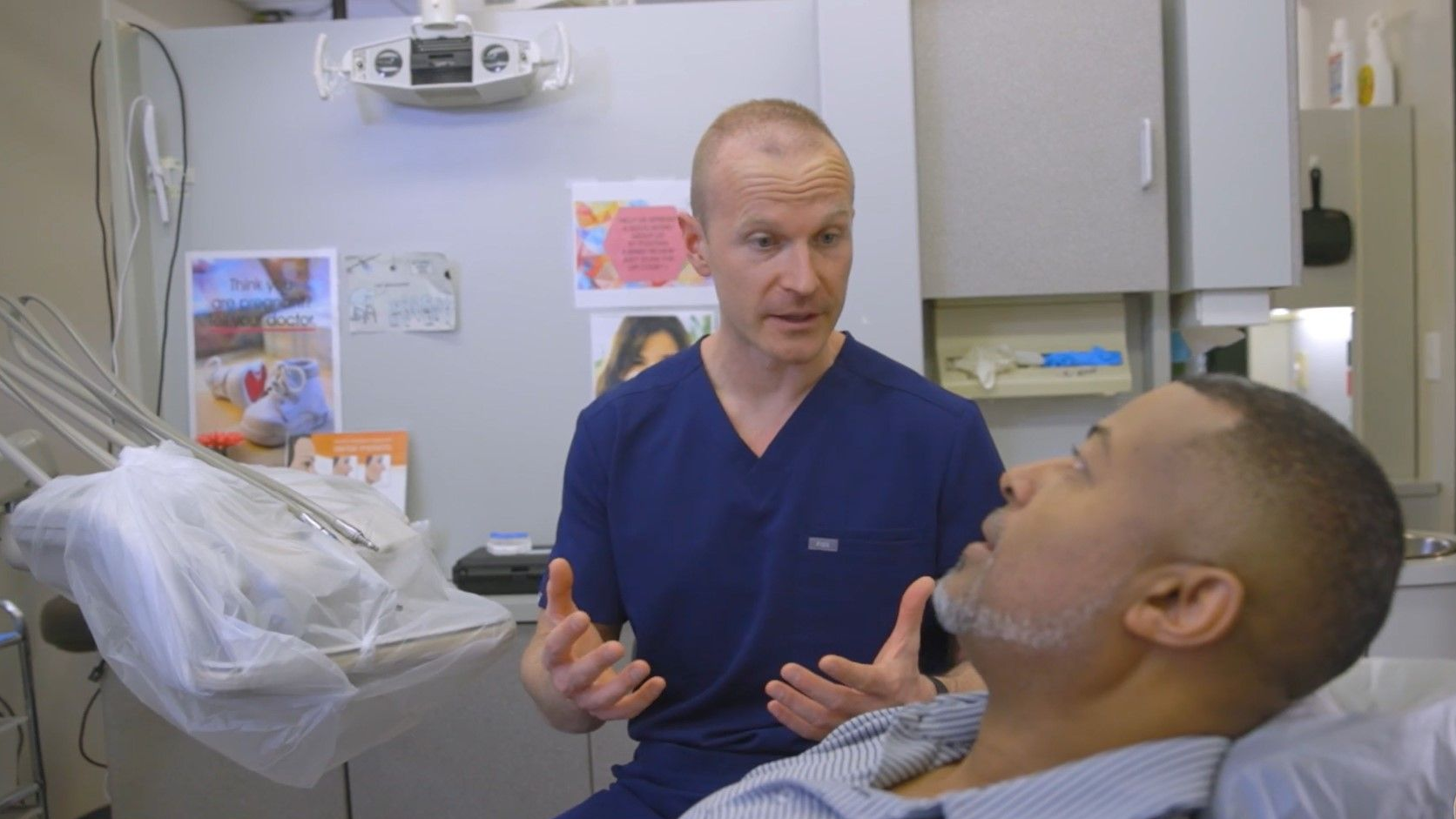 A man is sitting in a dental chair talking to a dentist.