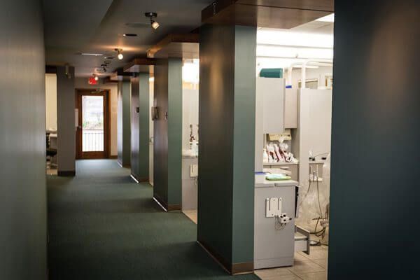 Hallway in dental office with teal walls, dental stations, and wooden trim.