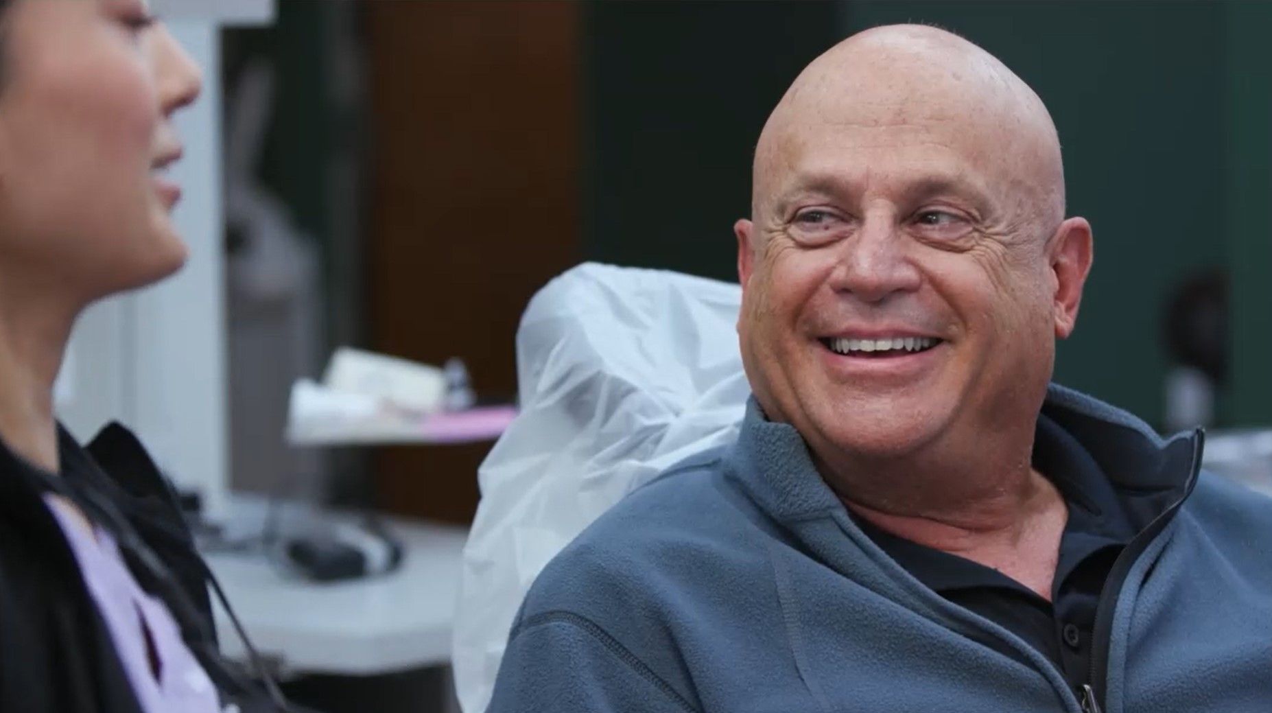 A man is smiling while sitting in a dental chair next to a woman.