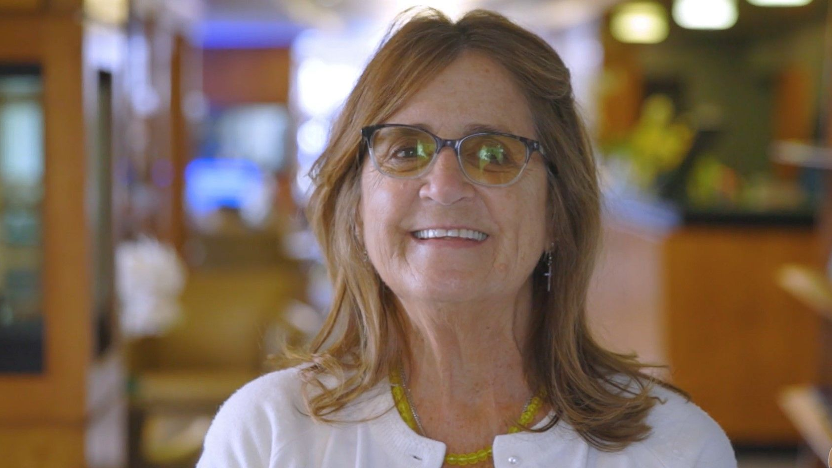 A woman wearing glasses and a white sweater is smiling for the camera.